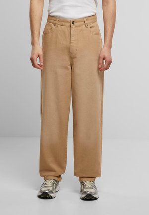 Beige wide-leg trousers made of cotton, featuring a front button closure, belt loops, and side pockets, paired with silver athletic shoes.