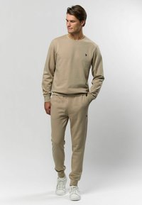 Sweatshirt bej și pantaloni jogger asortați, fabricate dintr-un material moale. Prezintă un logo mic brodat pe piept și manșete și talie ribbate.