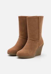 Bottes à talon compensé marron en suède synthétique avec une texture lisse et des détails cousus ; bout arrondi et tige courte.