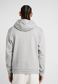 Sweat à capuche gris avec une texture douce. Comprend une poche kangourou, des poignets et un ourlet côtelés. Vue de dos mettant en valeur la forme de la capuche.