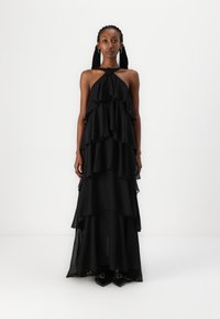 Rochie neagră, fluidă, cu bretele halter, având volane suprapuse și o textură semi-transparentă, cu un detaliu în formă de nod la guler.