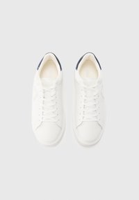 Ζευγάρι λευκά sneakers με κορδόνια και μπλε ταμπελάκι στη φτέρνα, σε λευκό φόντο, από πάνω.