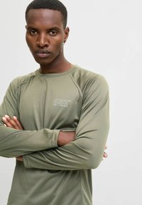 Olijfgroene long-sleeve performance shirt met een gestructureerde stof, raglanmouwen en een klein "CNZ" logo op de borst.