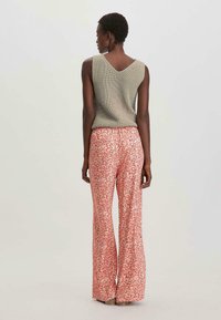 Olijfgroen gebreid mouwloos topje met v-hals; flare, gestreepte broek in een roze en witte bloemenprint met een zachte textuur en brede pijpen.