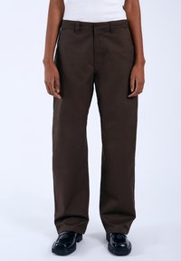 Bruine, rechte pantalons van katoen, met een plat front en riemlussen. Gekozen met zwarte schoenen, gladde textuur, minimale details.