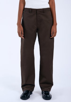 Bruine, rechte pantalons van katoen, met een plat front en riemlussen. Gekozen met zwarte schoenen, gladde textuur, minimale details.