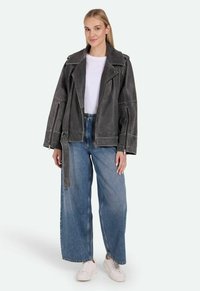 Hallux hallituksen nahkavöö ja lai krae ning asümmeetriline esi tõmblukk. Ühendatud laia lõikega siniste denim pükstega ja valgete pandaadega.