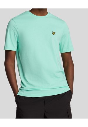 Homme portant un t-shirt à manches courtes turquoise clair avec un petit logo d'oiseau jaune sur la poitrine, associé à un short cargo noir.