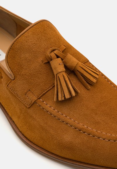 Suede loafers in tan with tassel accents. Features a rounded toe, stitched detailing, and a smooth leather lining.