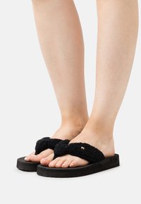 Black fabric slide sandals with a cross-strap design, textured surface, and black rubber sole. Exposed toes on a neutral background.