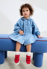 Lyseblå denimkjole med blomsterprint, knaplukning og en Peter Pan-krave; kombineret med røde velcrosneakers og hvide flæsestrømper.