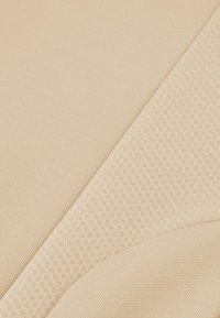 Tejido beige con superficies texturizadas que presentan un pequeño patrón de panal y áreas lisas, creando un contraste en el diseño y la textura.
