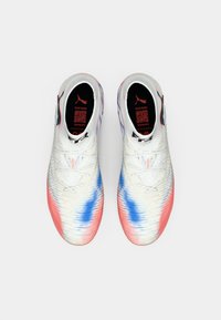 Par van witte sportschoenen met rode en blauwe accenten, vetersluiting, en zichtbare zwarte binnenzolen met rode tekst en logo's.