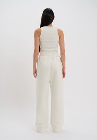 Witte geribde tanktop gecombineerd met losse, lichte, crèmekleurige sweatpants. De kledingstukken hebben een relaxte pasvorm en een elastische tailleband.
