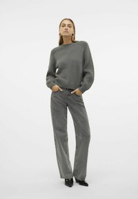Pullover grigio a costine con scollo rotondo e maniche lunghe, abbinato a jeans grigi a vita alta e gamba larga, con tacchi neri lucidi.