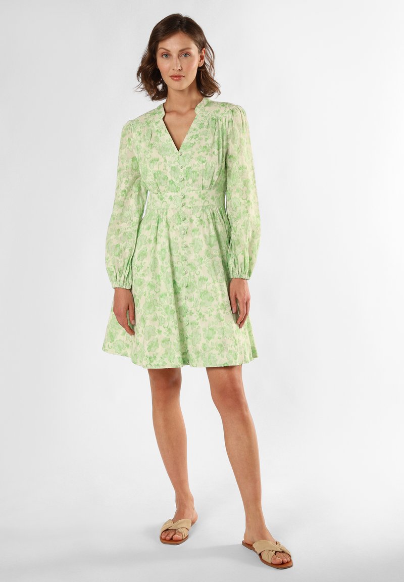 Green floral dress with long sleeves, V-neck, and waist tie. Made of lightweight fabric with a flared skirt, paired with beige sandals.