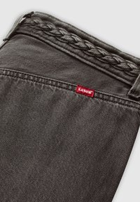 Gros plan sur un tissu en denim gris foncé avec un détail tressé et une petite étiquette rouge Levi's cousue près de la couture supérieure.