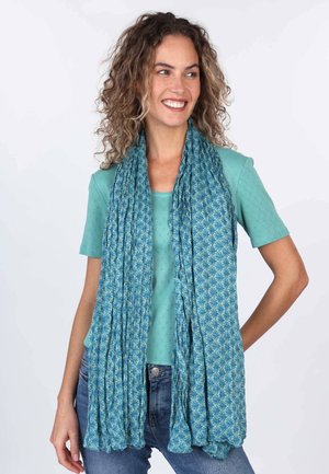 Lightweight, patterned scarf in teal with intricate designs; pleated texture adds dimension. Worn over a matching top and jeans.