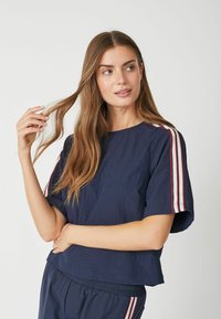 Navyblauwe T-shirt met korte mouwen en een losse pasvorm, voorzien van witte en rode gestreepte accenten op de schouders en een textielstructuur.