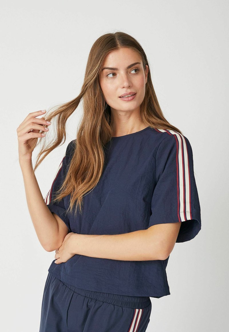 Navyblauwe T-shirt met korte mouwen en een losse pasvorm, voorzien van witte en rode gestreepte accenten op de schouders en een textielstructuur.