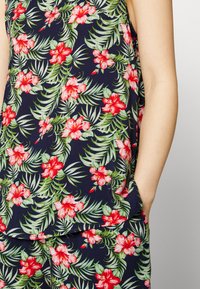 Top com estampa floral em azul-marinho com flores de hibisco vermelhas e folhas verdes. Apresenta um corte solto e bolso lateral. Tecido macio e leve.