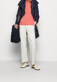 Cappotto imbottito blu navy, maglione a maglia corallo, pantaloni bianchi a gamba larga e mocassini panna. Accessorio: borsa trapuntata blu navy con tracolla.
