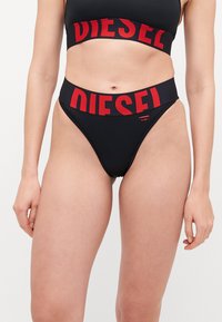 Fekete bikini szett, amely crop topból és magas derekú alsóból áll. Merész piros "DIESEL" logó az elasztikus deréknál. Simább, rugalmas anyag.