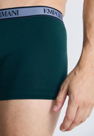 Grüne Baumwoll-Boxershorts mit einem grauen Bund, der das Logo "EMPORIO ARMANI" trägt. Der Stoff ist glatt und hat eine figurbetonte Passform.