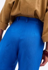 Blauwe high-waisted broeken van een gladde stof, met zijzakken en een getailleerde pasvorm, gecombineerd met een bruine, gestructureerde top.