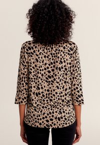 Leopardenmuster-Oberteil in Beige und Schwarz, aus weichem Stoff mit 3/4-Ärmeln, runder Ausschnitt und lockerer Passform.