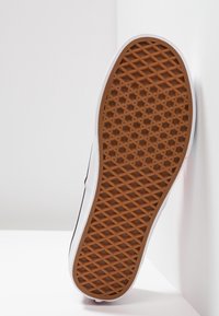 Braune Gummisohle mit einem Rautenmuster, weißen Seitenwänden und einer leichten Krümmung. Das Design ist schlicht, ohne sichtbare Logos oder Muster.