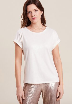 Weißes T-Shirt mit kurzen Ärmeln und umgeschlagenen Bündchen, aus einem weichen Stoff mit leichtem Glanz, kombiniert mit glänzenden metallisch goldenen Hosen.