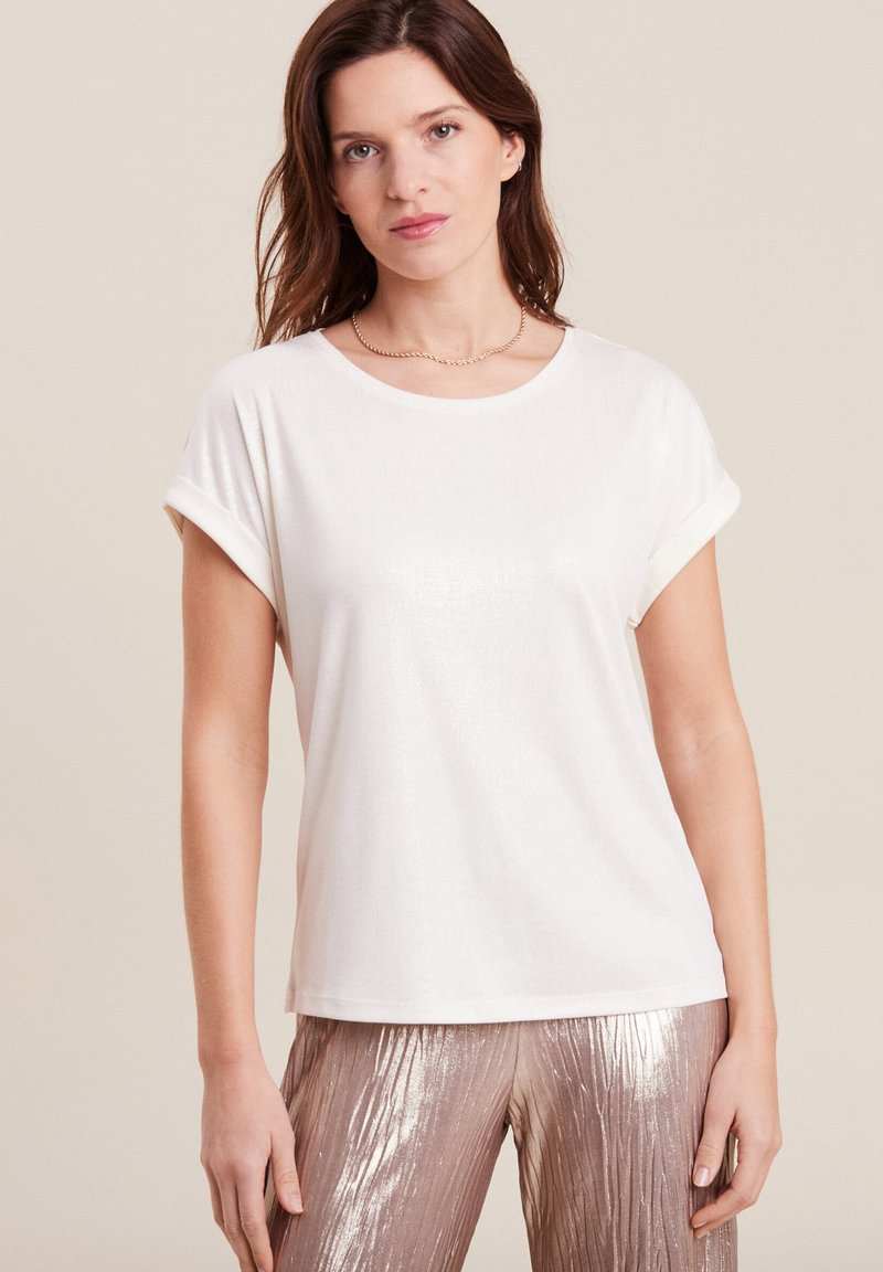 Witte T-shirt met korte mouwen en opgerolde mouwen, gemaakt van een zachte stof met een subtiele glans, gecombineerd met glanzende metallic gouden broek.
