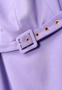 Lavendelfarbenes Stoffmaterial mit glatter Textur, ausgestattet mit einer quadratischen Schnalle und goldfarbenen Beschlägen an einem Gürtel-Detail. Das Design beinhaltet Ösen zur Anpassung.