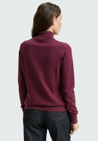 Maglione a collo alto bordeaux con scollo e polsini a coste, realizzato in materiale morbido. Abbinato a jeans scuri, con cuciture ben definite.