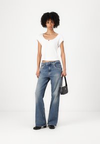 Hvit ribbet crop top med bølgete kanter, blå vide jeans, svarte hæler og en liten svart crossover-veske.