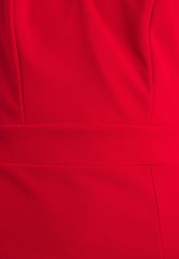 Röd klänning i mjukt tyg med en slät yta, med en strukturerad passform och en väldefinierad midja. Sömlinjer skapar subtila designelement.