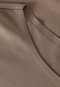 Tessuto marrone con una texture liscia, caratterizzato da un design a V e cuciture visibili lungo i bordi. Materiale morbido e flessibile.