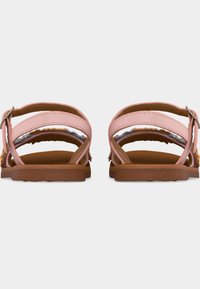 Ζευγάρι ροζ επίπεδων σανδαλιών με λουριά στον αστράγαλο και καφέ σόλες, εμφανιζόμενα από πίσω σε λευκό φόντο.
