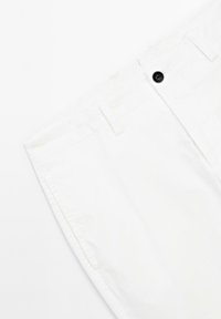 Witte katoenen broek met een zwarte knop, een rechte snit en riemlussen. De stof heeft een zachte textuur met minimale stikdetails.