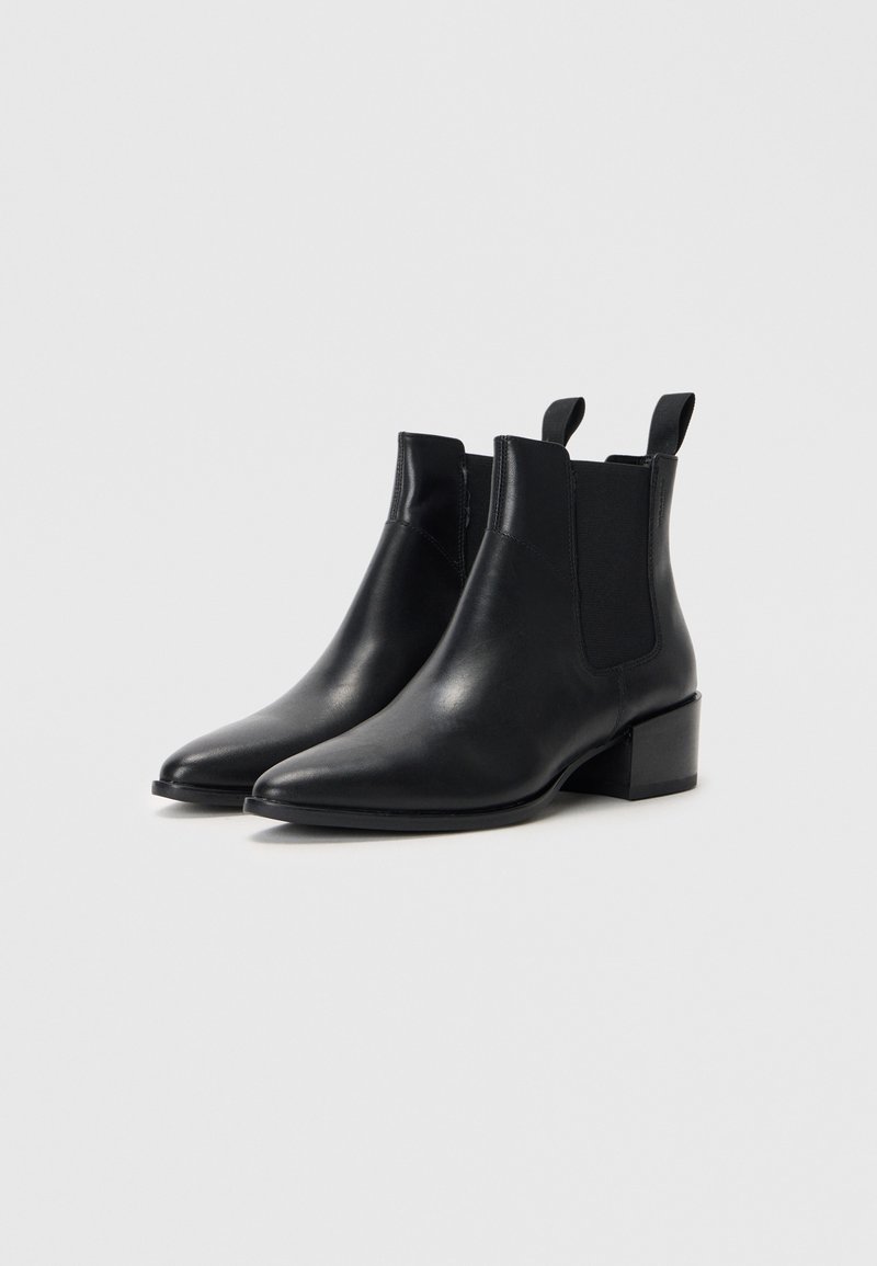 Bottines en cuir noir avec un bout pointu, des panneaux élastiques sur les côtés et des tirettes. Elles ont un petit talon carré et une texture lisse.