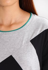 Närbild av en person som bär en grå och svart flerfärgad skjorta med en grönkantad rund halsringning och synlig nyckelben.