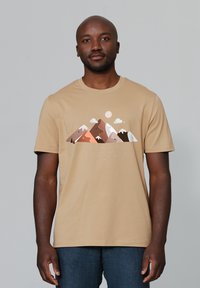 Beige T-Shirt aus weicher Baumwolle, mit einem Bergmotiv in verschiedenen erdigen Farbtönen und einer dezenten Darstellung von Wolken und Sonne.