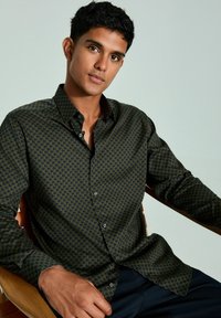 Dunkelblaues Langarmshirt mit geometrischem Muster in Gold. Verfügt über einen spitzen Kragen und einen Button-Front-Design. Glatte Stofftextur.