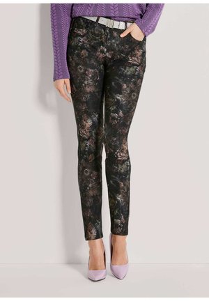 Personne portant un pantalon slim foncé à motifs floraux avec une ceinture argentée, un pull violet en maille torsadée et des talons aiguilles pointus violet clair.