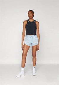 Black sleeveless crop top paired with light blue drawstring shorts. Textured fabric with Nike logo on chest and shorts. White athletic sneakers.