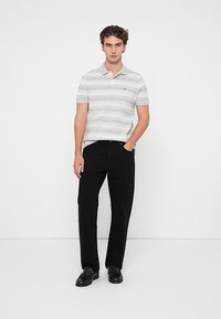 Tricou polo în dungi, de culoare gri deschis și alb, din bumbac, cu guler și mâneci scurte; asortat cu pantaloni negri închisi și pantofi negri.
