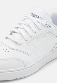 Baskets blanches Puma avec lacets blancs, logo embossé sur le côté, étiquette "PUMA SINCE 1948" sur la languette, et semelle en caoutchouc texturée.