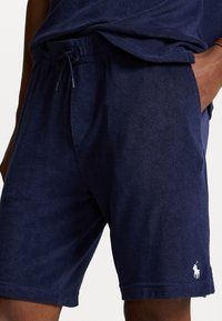 Marinblå shorts i mjukt tyg, med elastiskt midjeband och dragsko samt en liten vit logotyp på nedre vänstra benet.