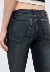 Κοντινό πλάνο ατόμου που φορά σκούρα μπλε τζιν παντελόνι με ορατές πίσω τσέπες και λευκό κοντό τοπ.